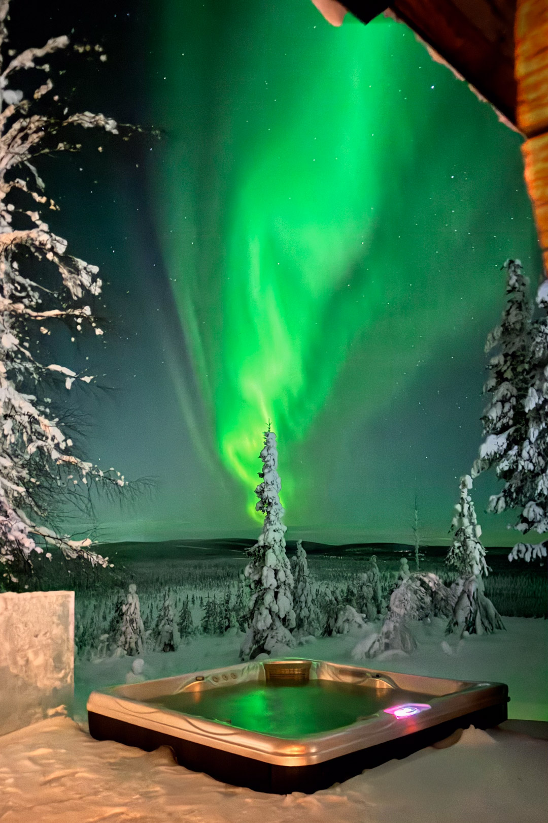 Aurore boréale verte au-dessus d'un jacuzzi extérieur et d'une forêt enneigée en Laponie finlandaise.
