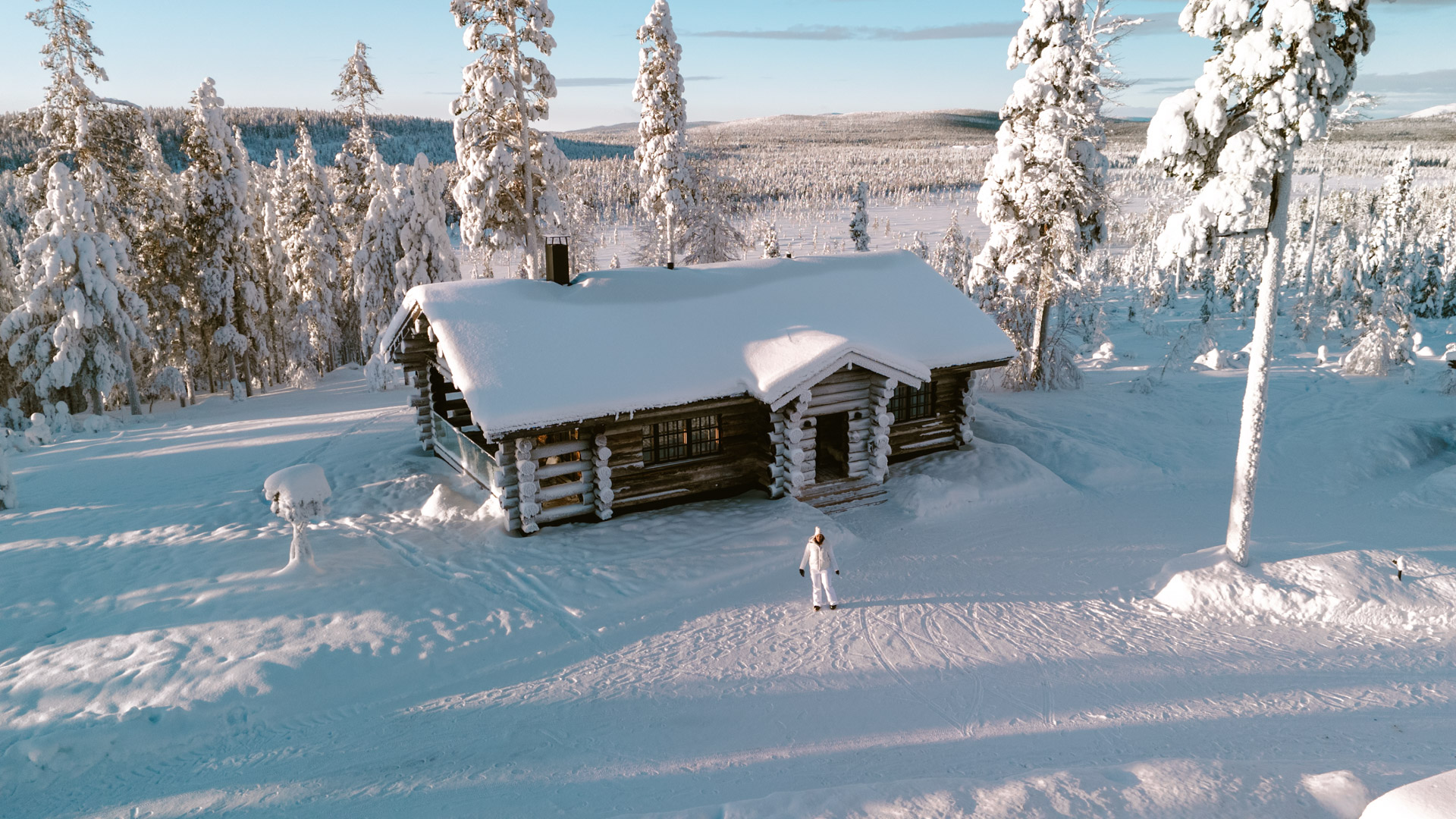 Chalet en bois entouré de sapins enneigés au cœur de la Laponie finlandaise en hiver.