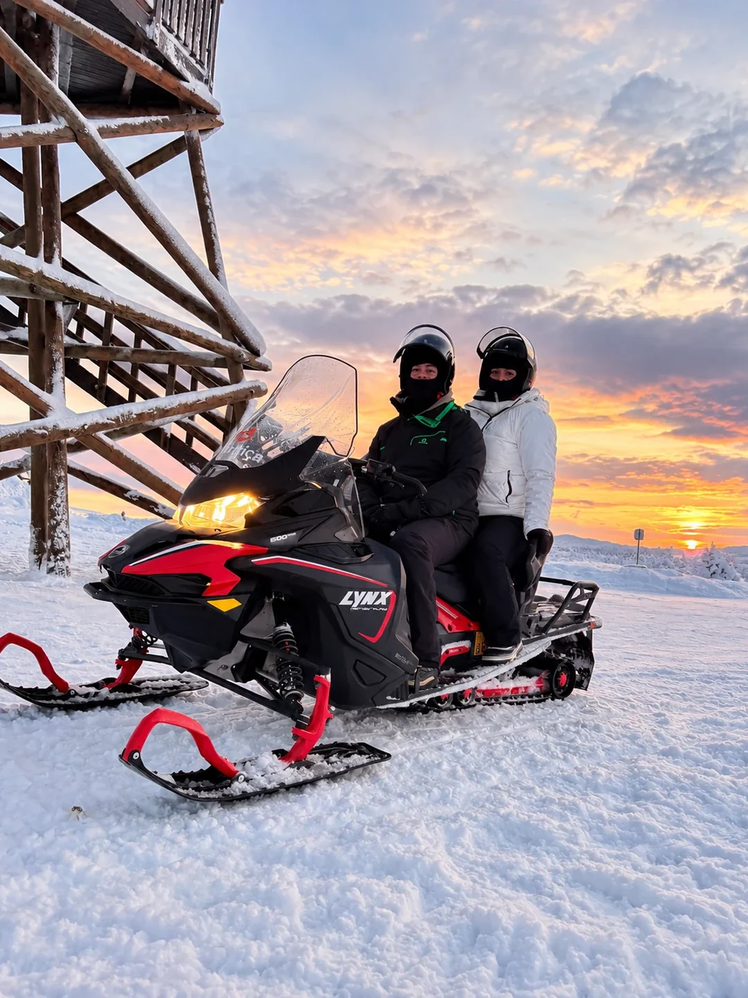 Florent et moi sur une motoneige en Laponie finlandaise, au milieu d’un paysage enneigé, au coucher du soleil.