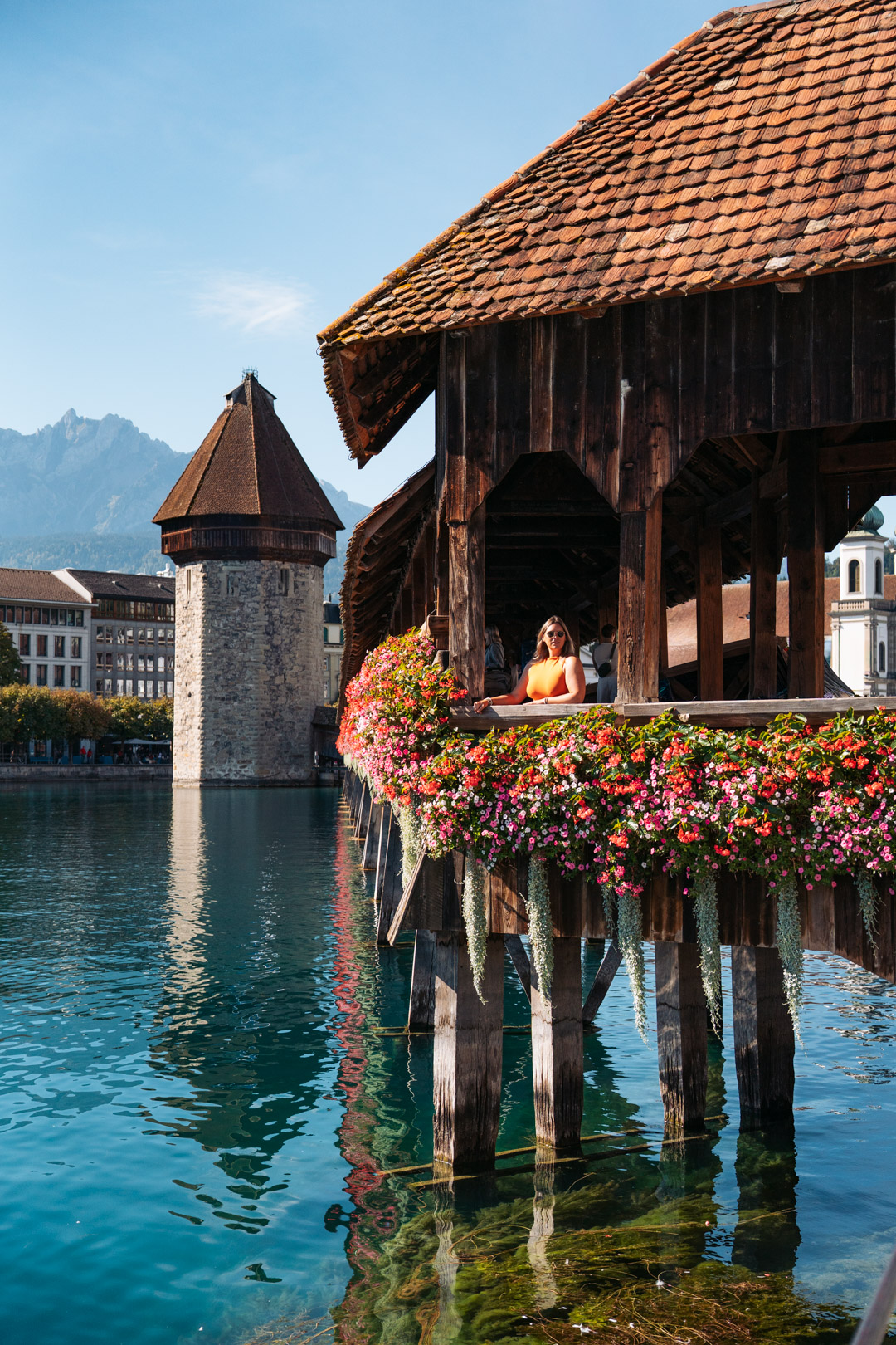 Pont de la Chapelle à Lucerne, décoré de fleurs, avec la tour de l’Eau et les montagnes en arrière-plan.