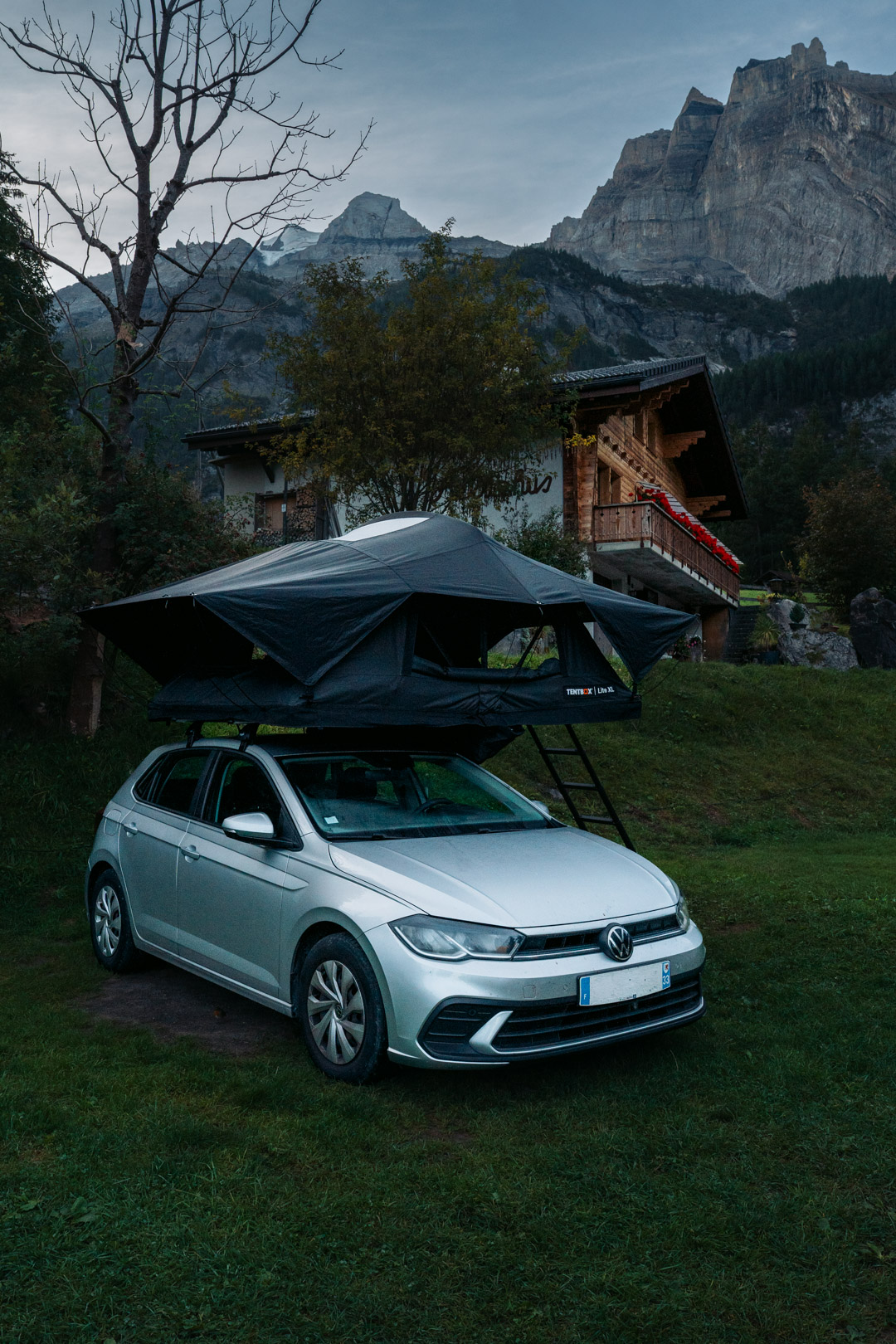 Tente de toit TentBox installée sur une voiture au pied des montagnes suisses, dans un camping entouré de chalets et de verdure.