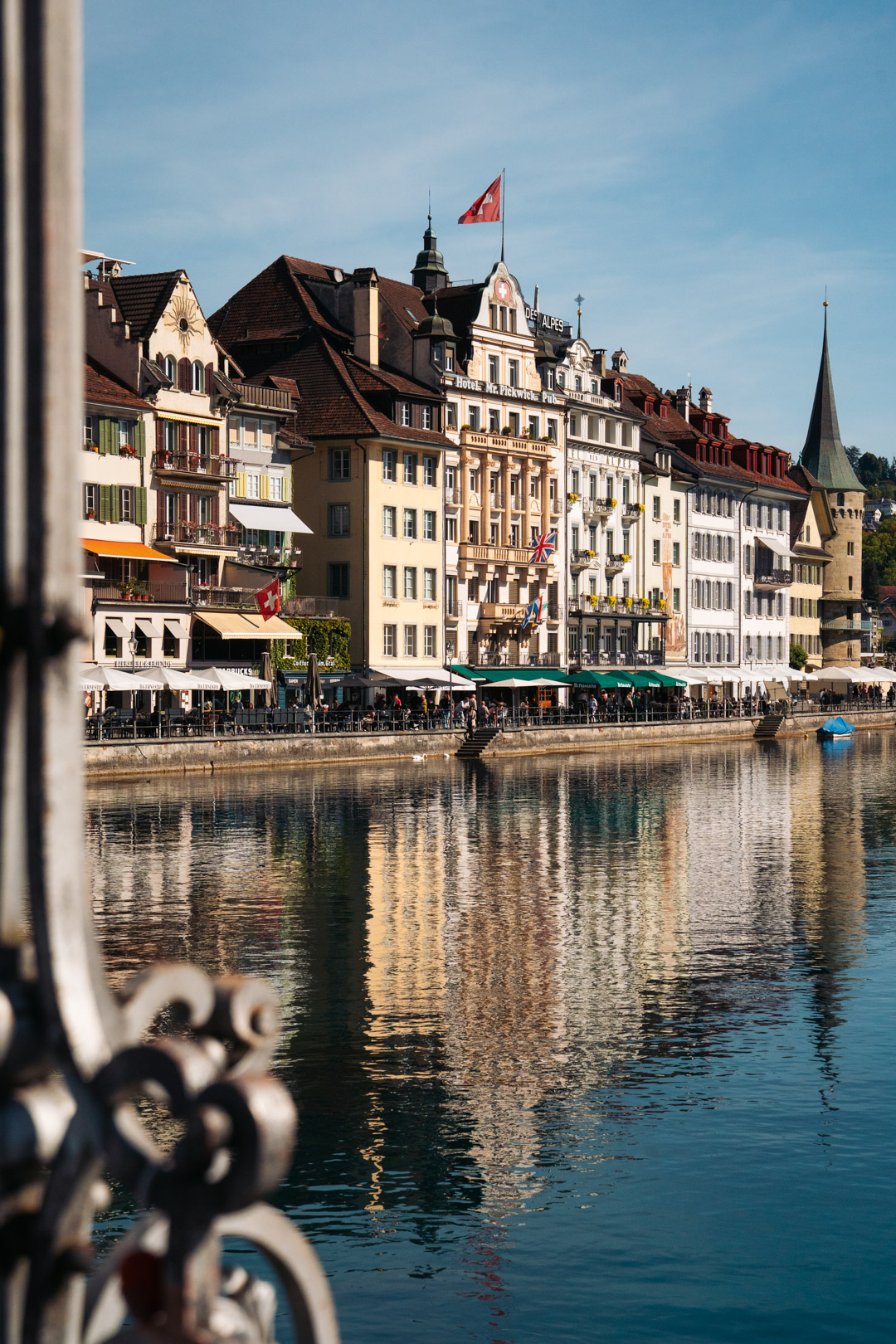 Façades historiques de Lucerne au bord de la rivière Reuss, avec leurs reflets dans l’eau et la tour de l’Hôtel de Ville en arrière-plan.