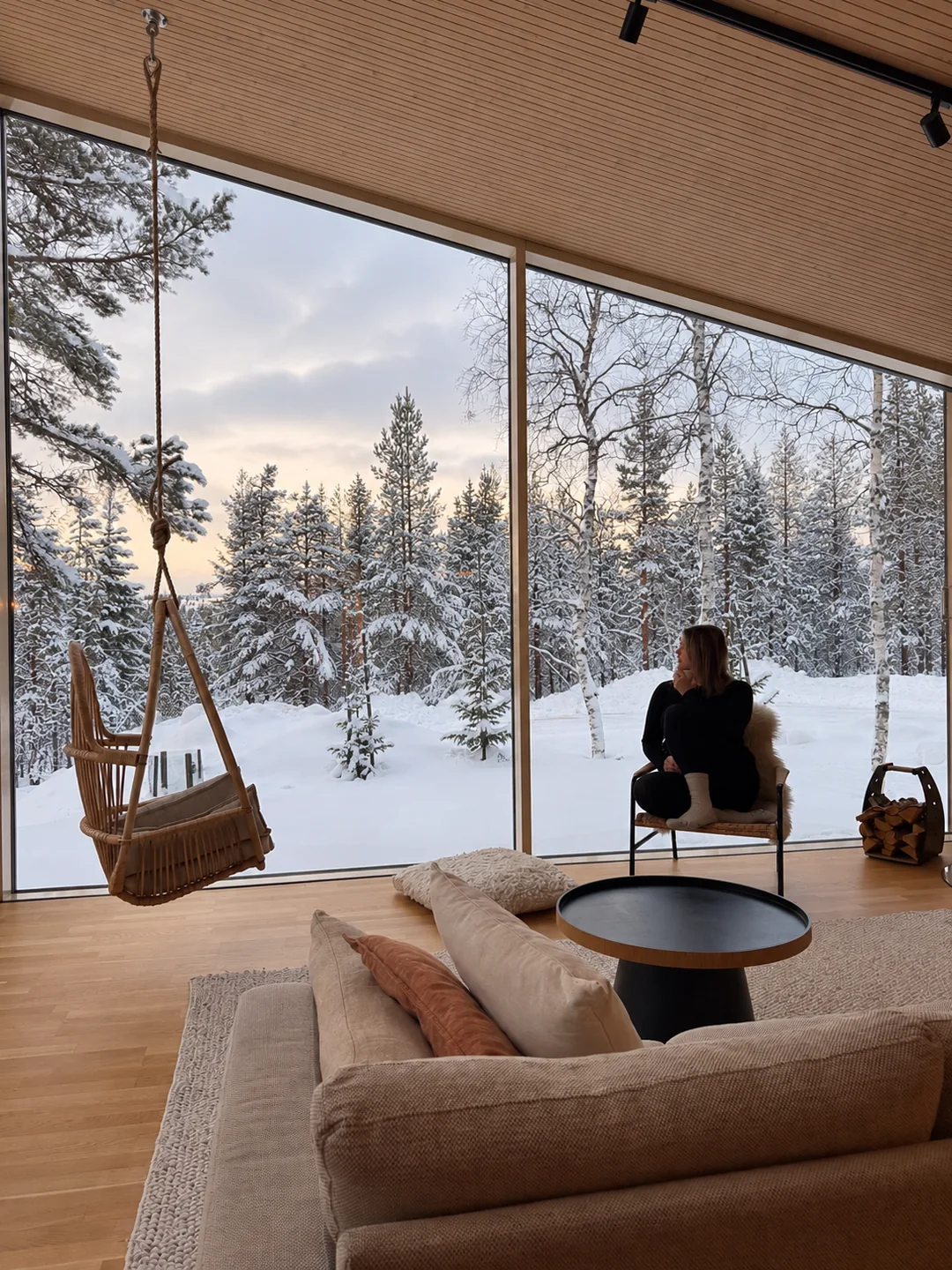 Vue sur une forêt de sapins enneigés depuis une villa en Laponie finlandaise, avec moi assise devant les grandes baies vitrées.