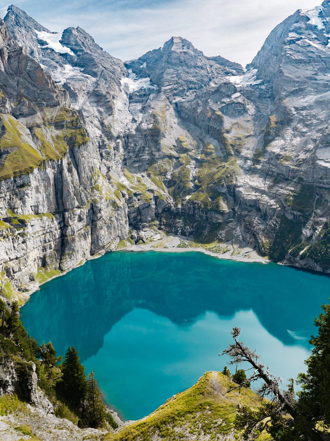 Vue plongeante sur le lac d’Oeschinensee aux eaux turquoise, entouré de hautes falaises grises et de glaciers dans les Alpes suisses.